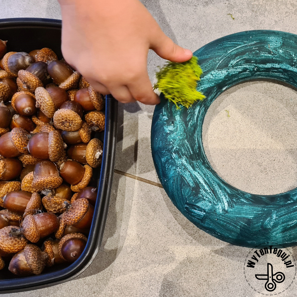 Sticking moss and acorns to the painted polystyrene wreath base